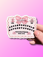 Kawaii Ouija Board sticker by Adorrible featuring cute ghost and spooky symbols on a black background.