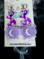 Adorrible Witch’s Cauldron Earrings featuring small black cauldron charms with silver accents, hanging from fishhook ear wires.