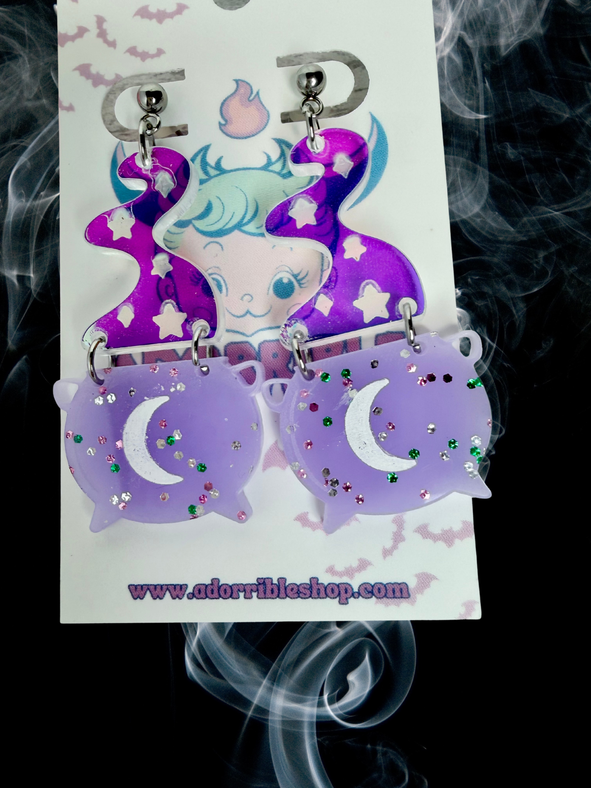 Adorrible Witch’s Cauldron Earrings featuring small black cauldron charms with silver accents, hanging from fishhook ear wires.