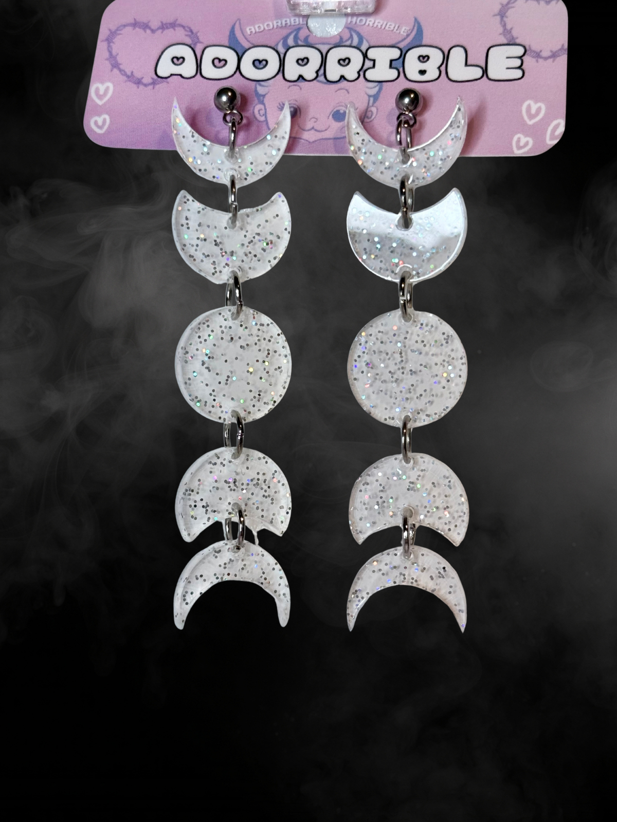 Adorrible moon phases earrings featuring silver crescent and full moon designs hanging from hooks.