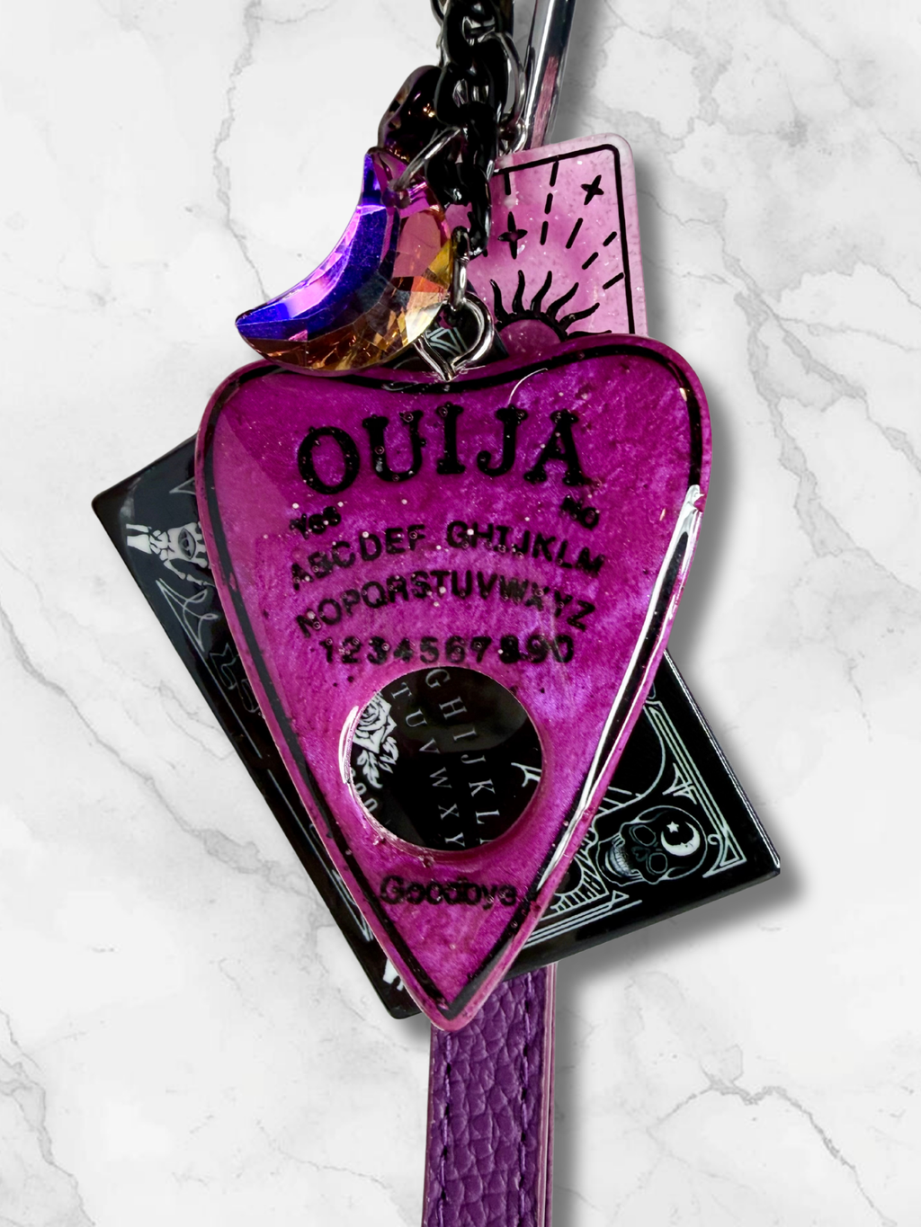 Adorrible Ouija Board keychain with wristlet and spooky charms, featuring a black Ouija planchette and charms for a spooky accessory.