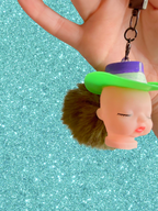 Adorrible Pride cowboy hat baby doll head keychain featuring a small doll head with colorful cowboy hat, keyring attached.