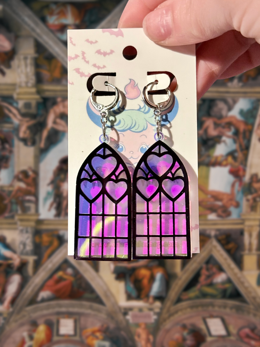 Adorrible Cathedral of Love acrylic dangle earrings with colorful, intricate design hanging from silver hooks.