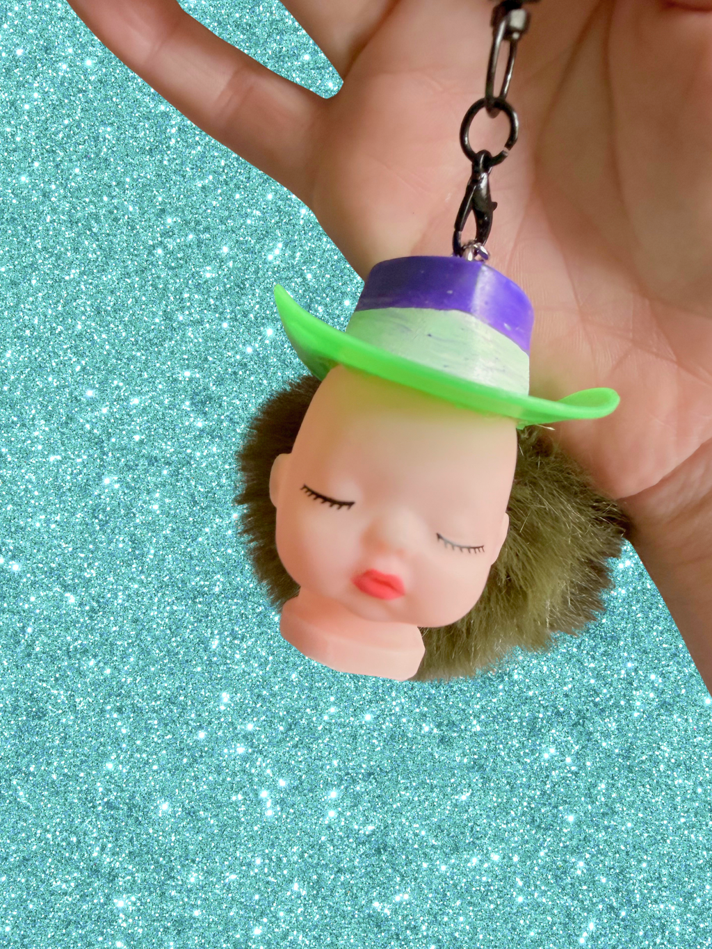 Adorrible Pride cowboy hat baby doll head keychain showing a small doll with a colorful cowboy hat attached to a keyring.