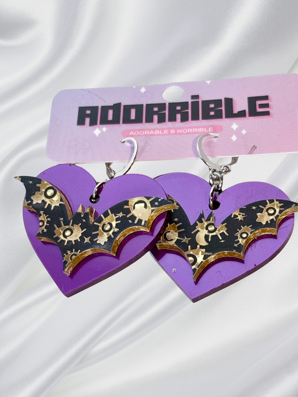 Adorrible Batty Heart earrings featuring black bat and heart design, showcased on display with a shiny surface.