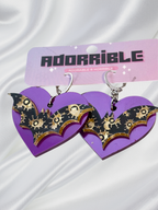 Adorrible Batty Heart earrings featuring black bat and heart design, showcased on display with a shiny surface.