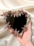 Decorative wall mirror with a heart-shaped frame made of barbed wire, stylish home decor piece by Adorrible.