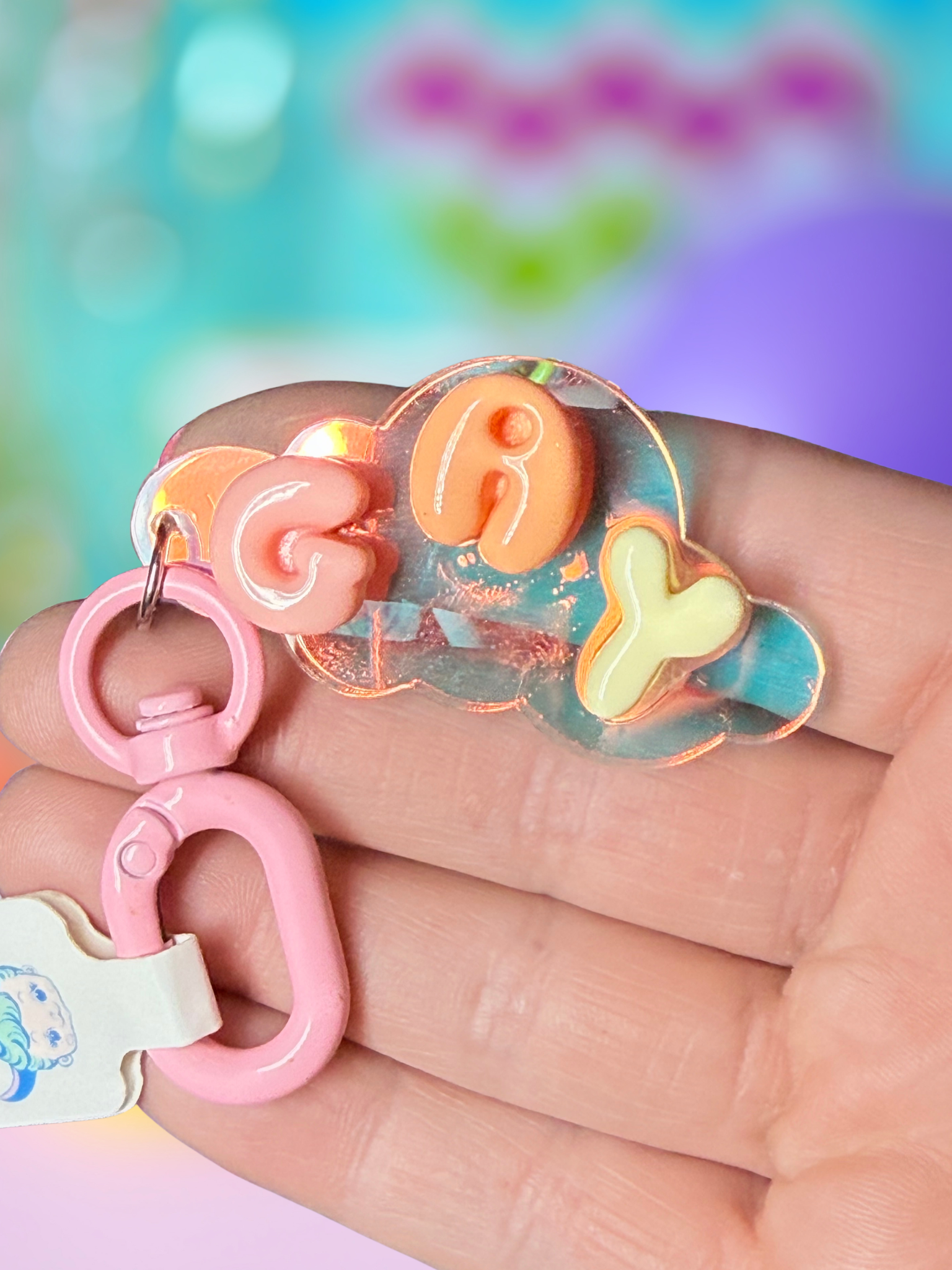 Iridescent cloud-shaped keychain with bubble letter design by Adorrible, featuring shiny, colorful finishes on a metal keyring.